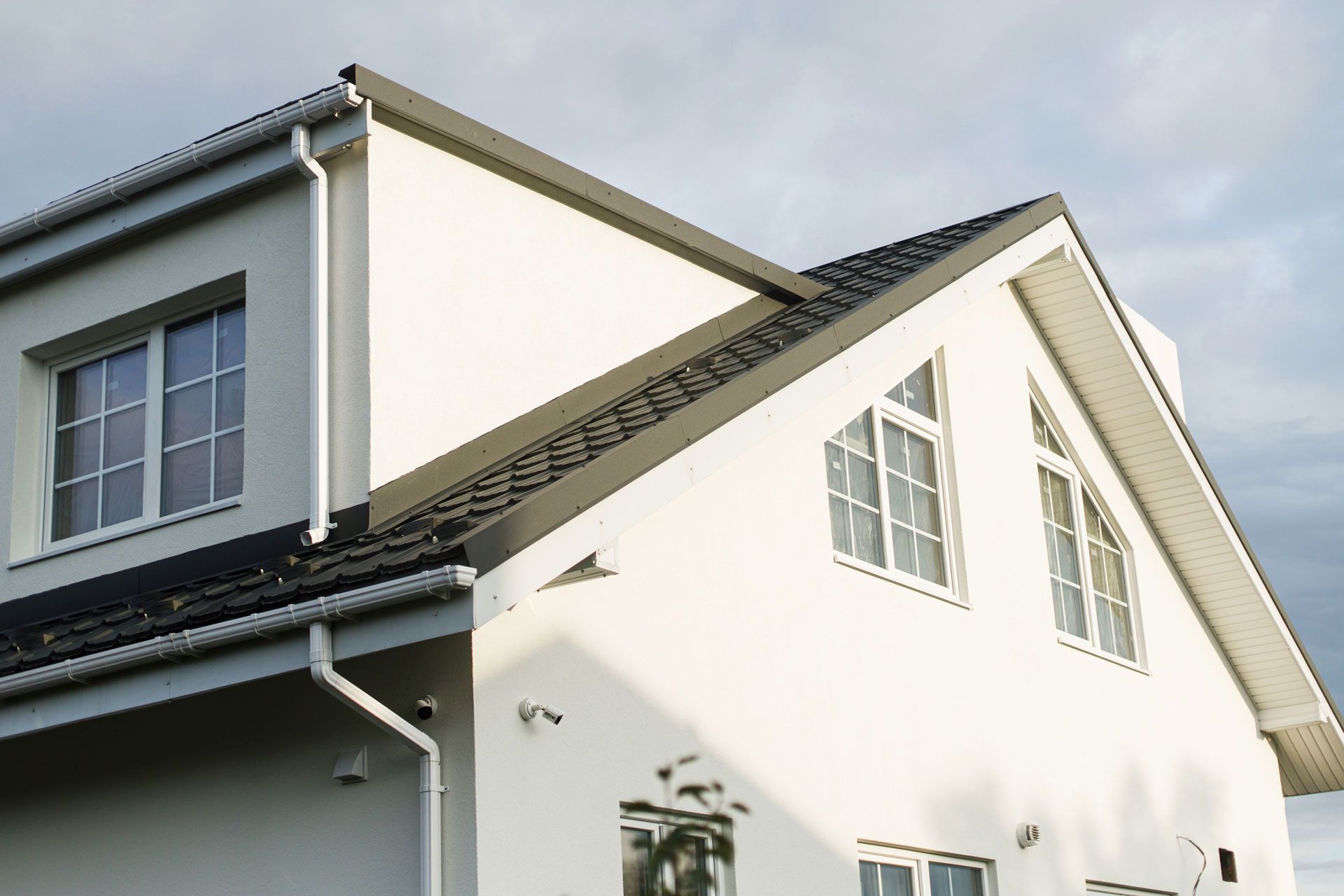 White two-story house with black roof, gutters, and windows against a cloudy sky.