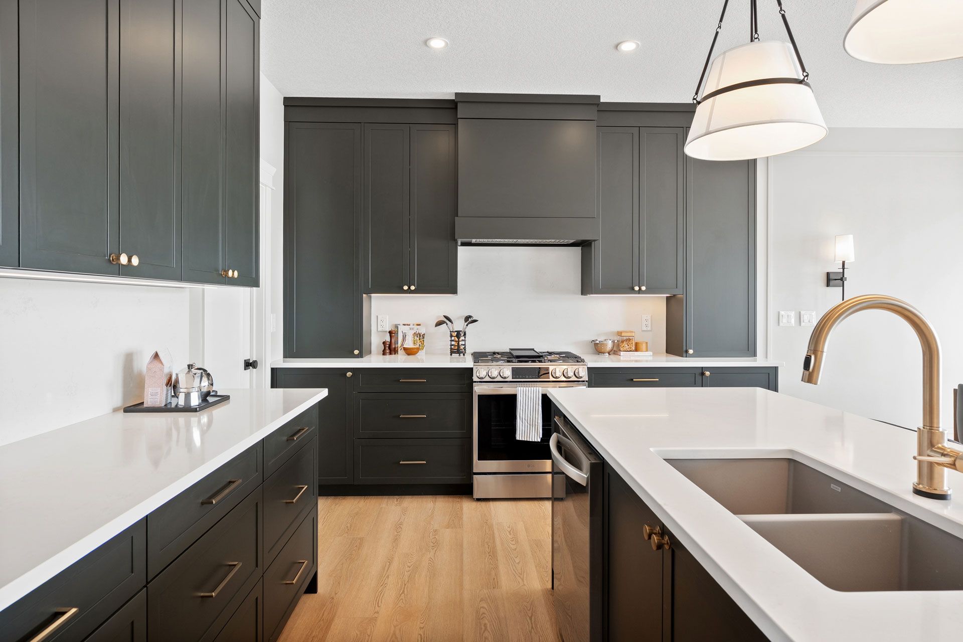 Modern kitchen with dark gray cabinets, white countertops, stainless steel appliances, and gold fixtures.