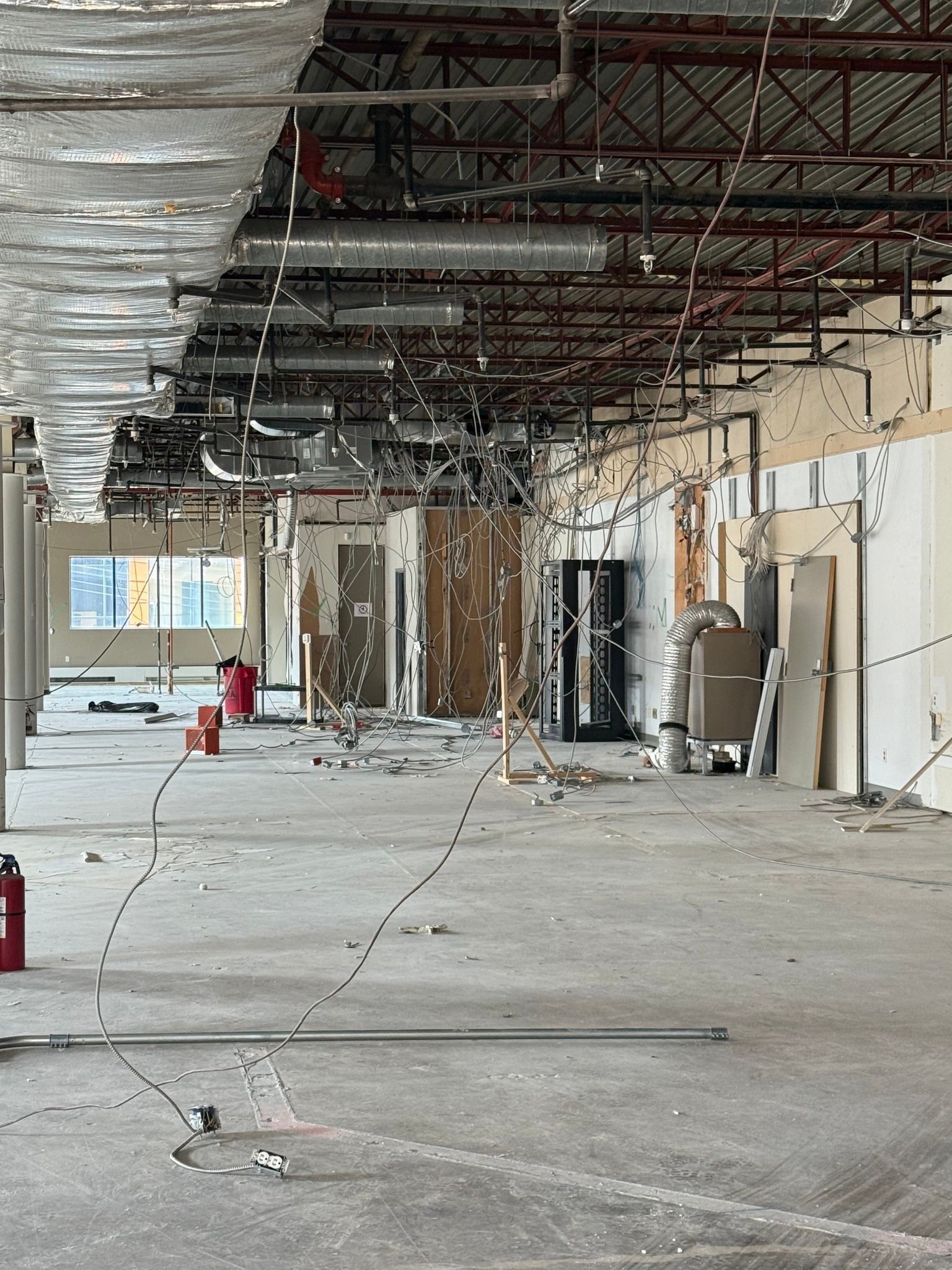 An interior view of a room under construction, showing an exposed ceiling, concrete floor, and debris-covered workspace.
