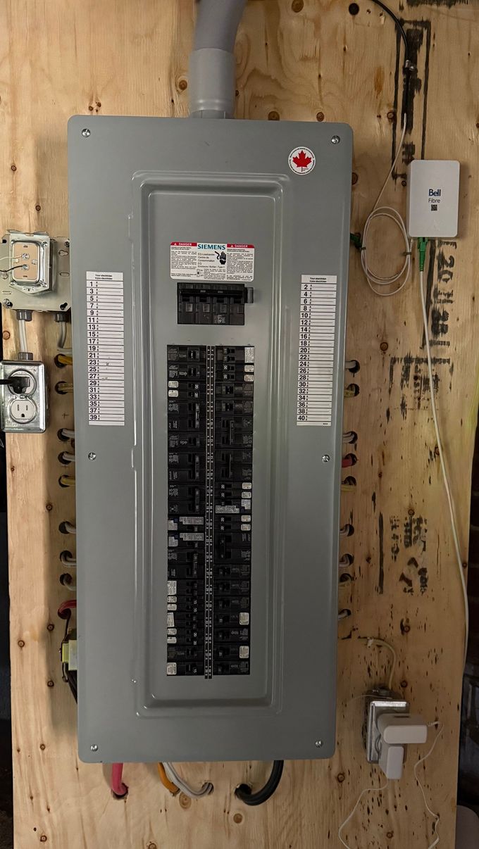 Un tableau électrique gris fixé sur un mur en bois, avec des prises électriques et des câbles visibles à proximité.