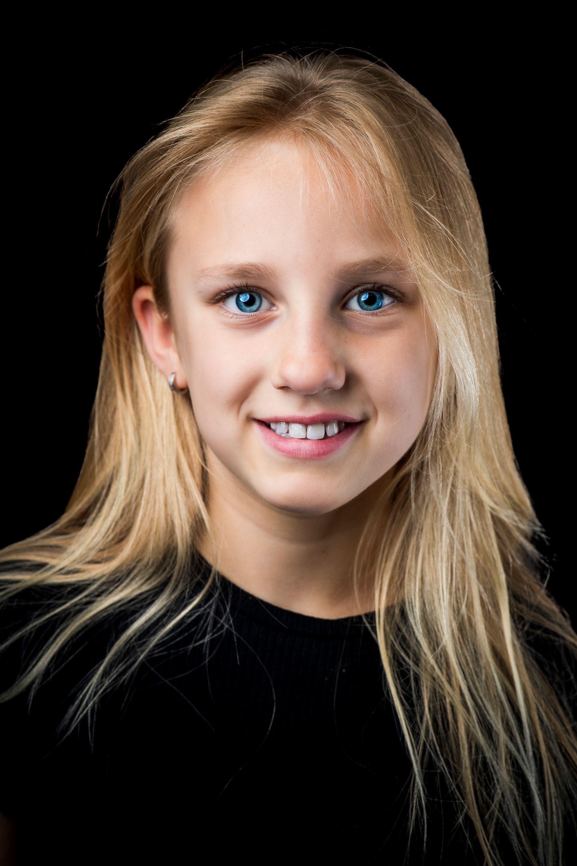 Een jong meisje met lang blond haar en blauwe ogen lacht naar de camera.