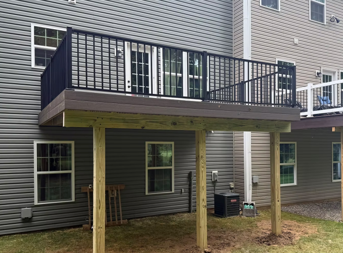 Back deck with black railing and stairs on a gray house, supported by wooden posts