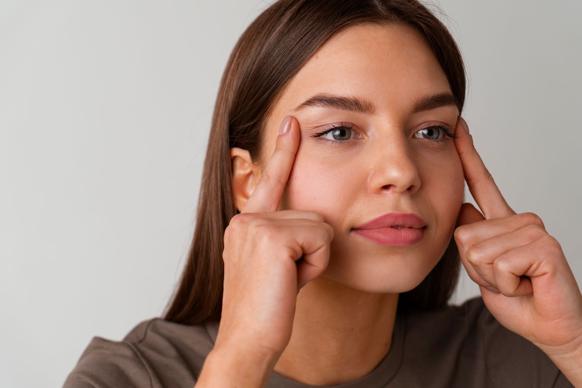 A woman is touching her eyebrows with her fingers.