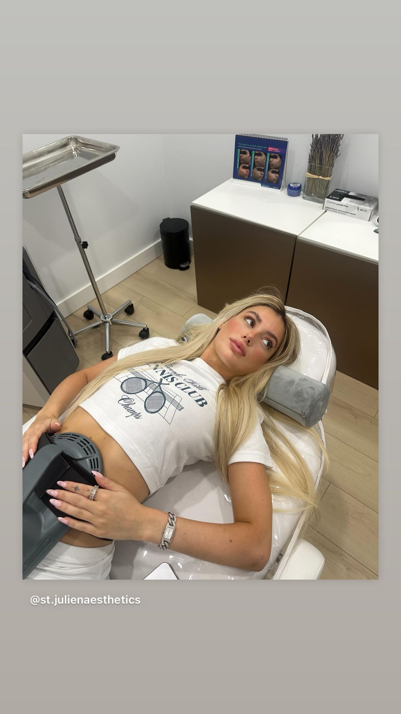 Blonde woman lying on a medical bed, wearing a white crop top. In a clinic setting.