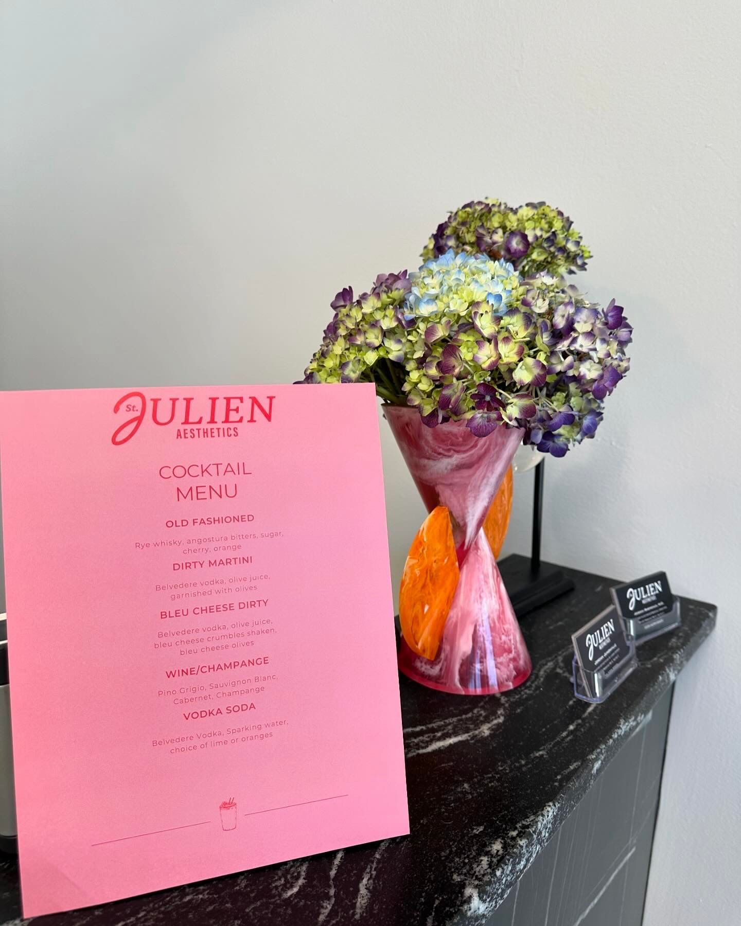Pink cocktail menu and vase of flowers on a marble counter.