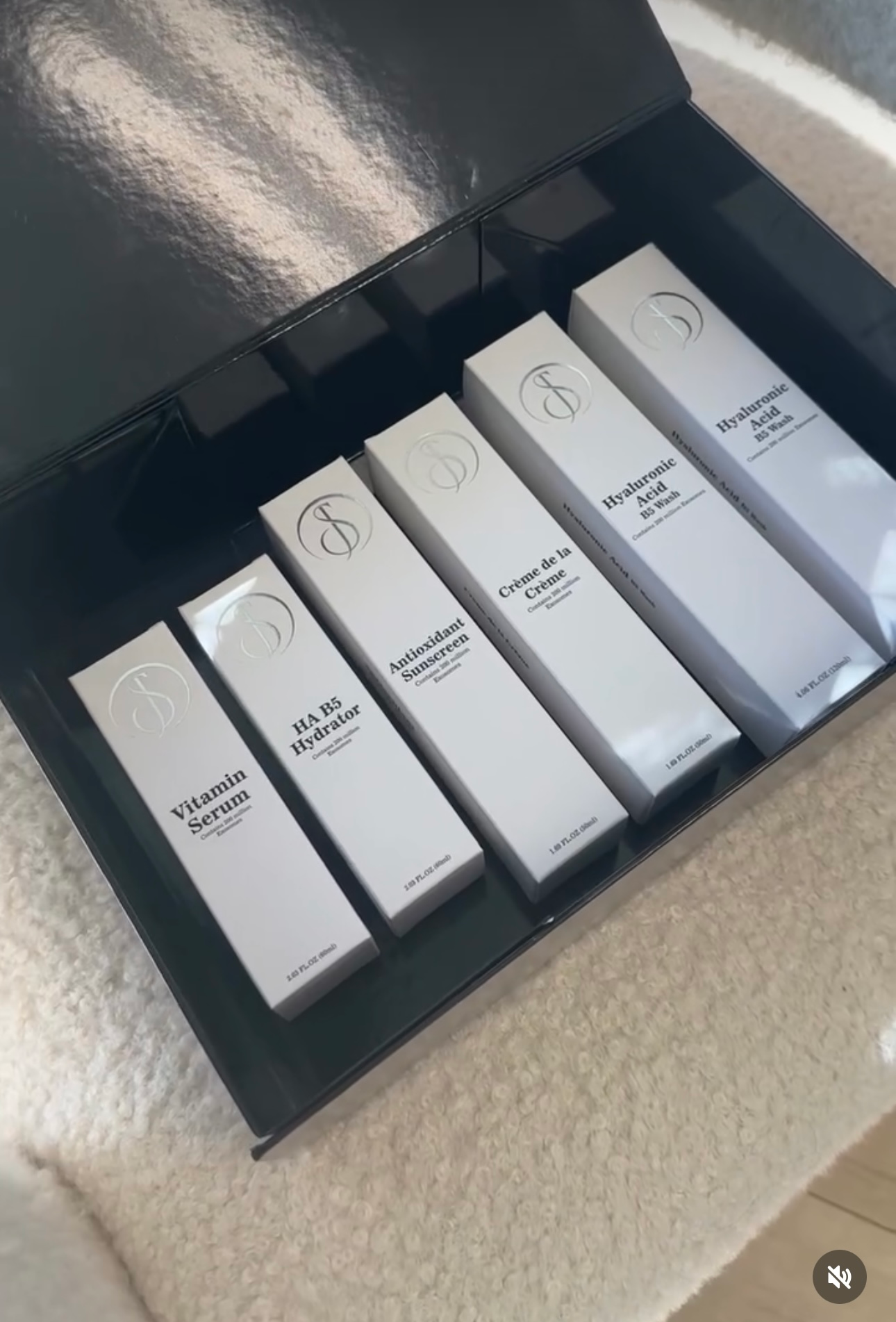 A box of white skincare product packages with black labels, sitting on a white surface.