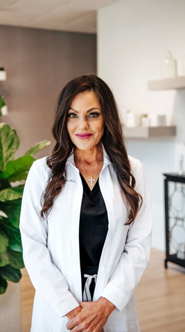 Man with crossed arms wearing black scrubs in a neutral-toned room with a plant.