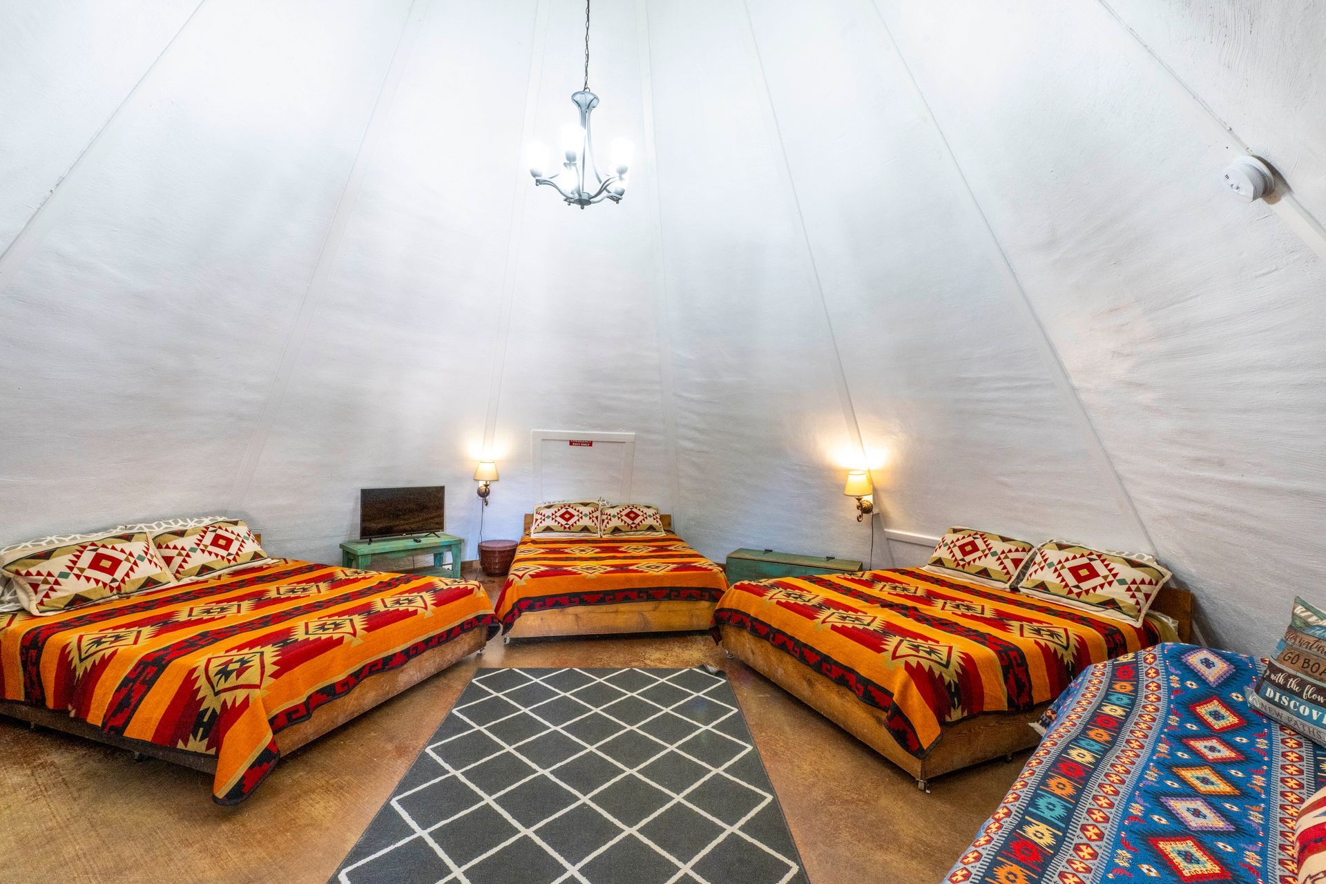 Interior of a large teepee with three beds, patterned blankets, a rug, and a chandelier.