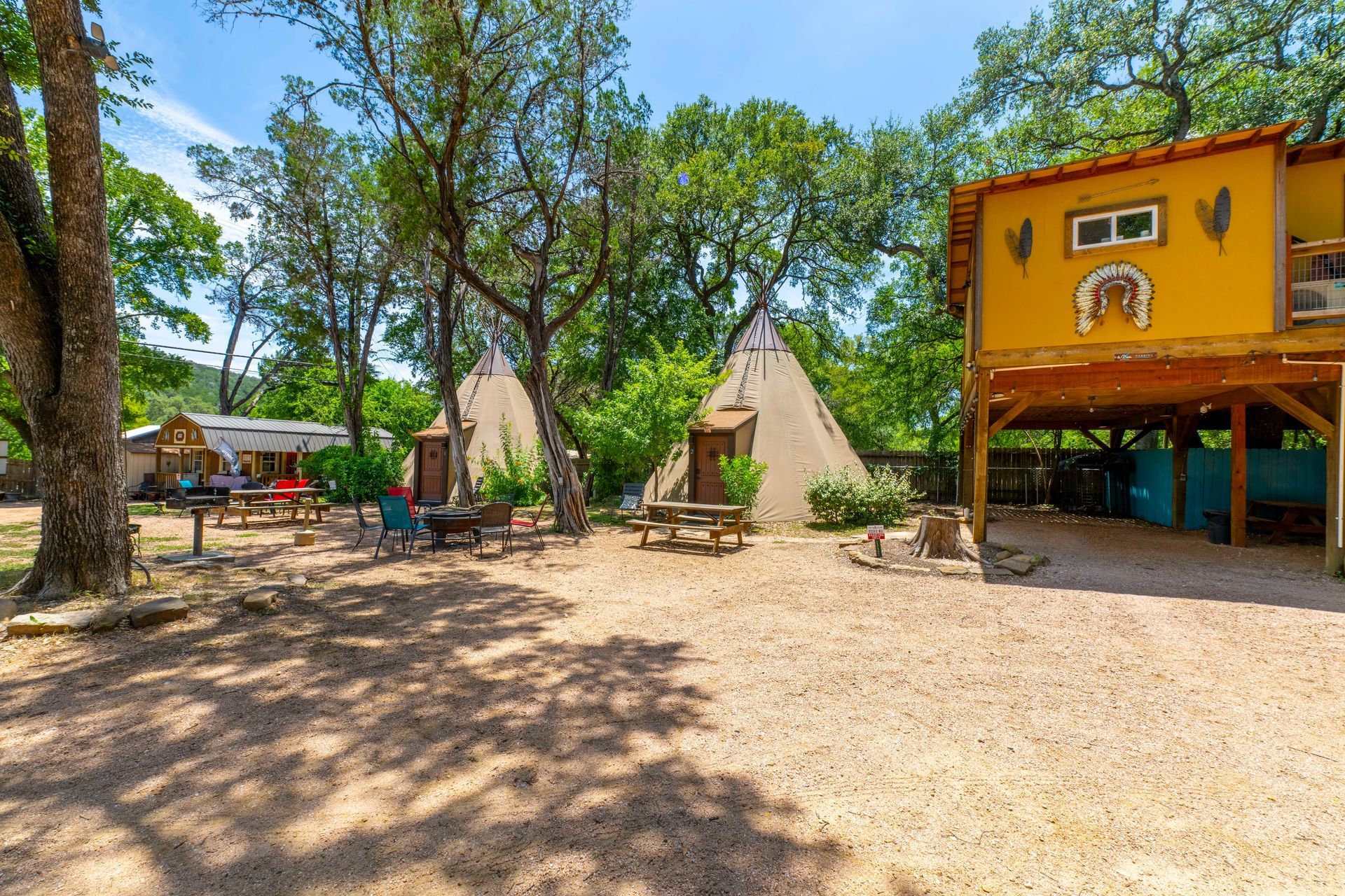 Campground with teepees, picnic tables, and a yellow elevated cabin under a blue sky.
