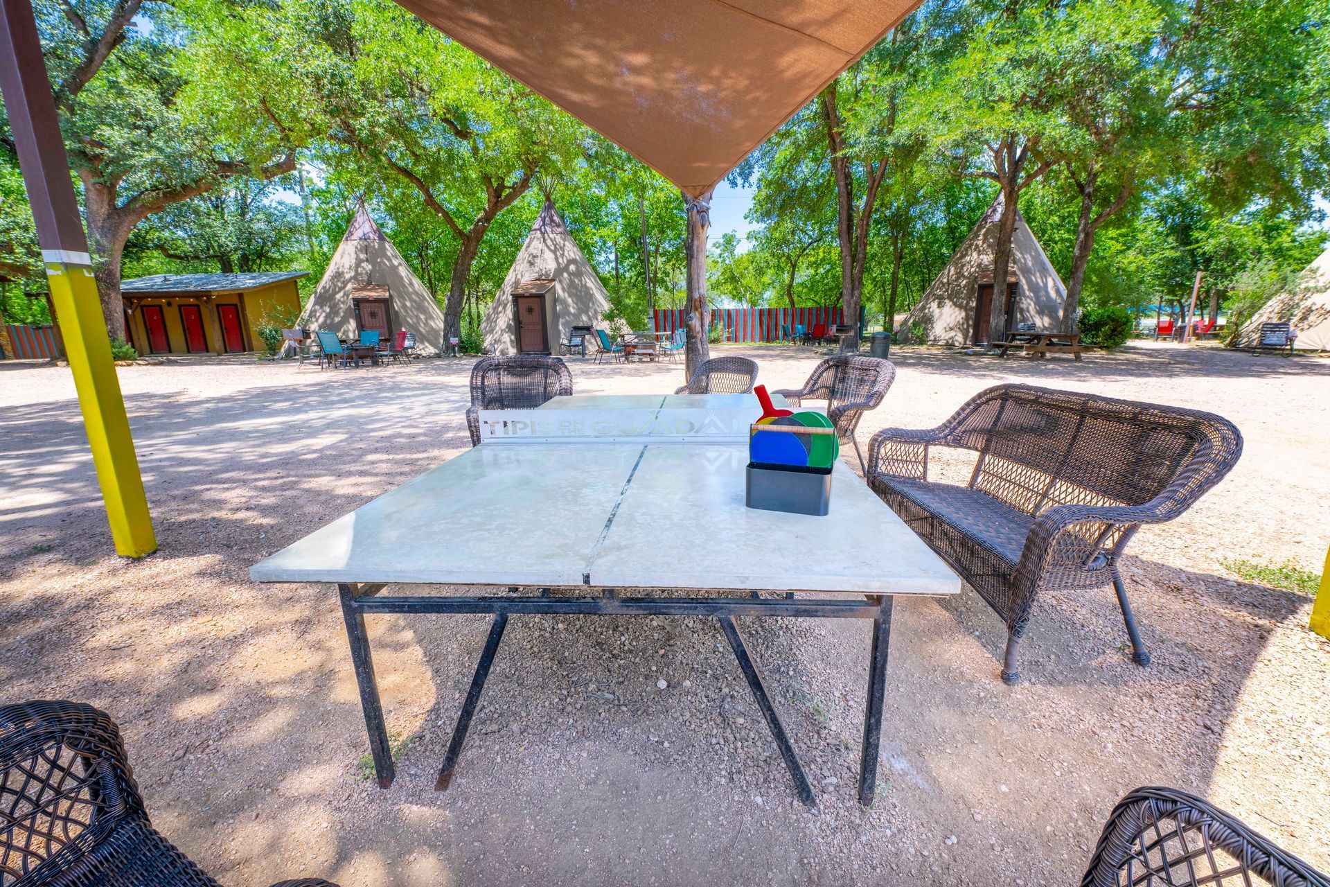 Ping pong table under a shade structure, with wicker chairs, teepee cabins in background.