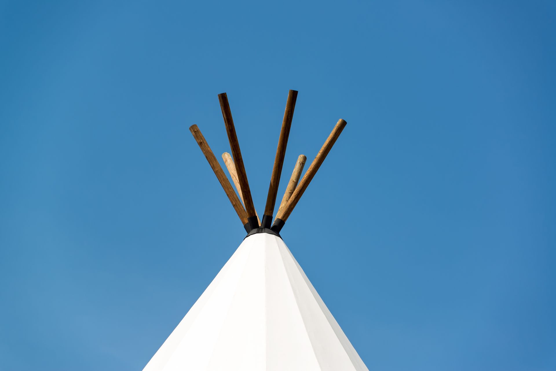 White teepee against a bright blue sky, with wooden poles extending from the top.
