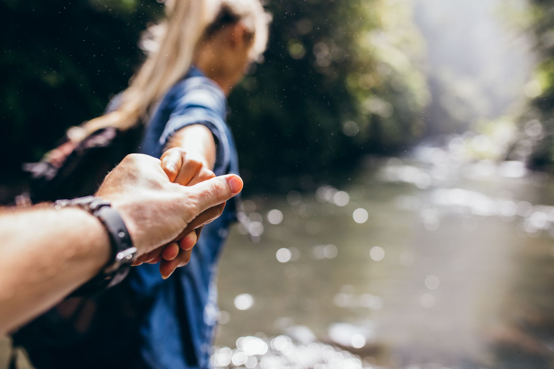 Couple holding hands, leading each other toward the river.