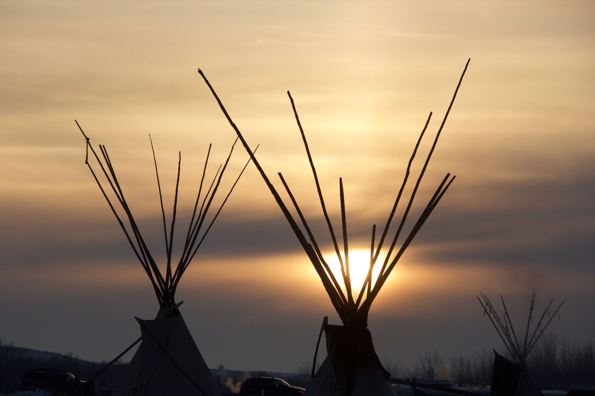 Silhouetted teepees against a golden sunset.