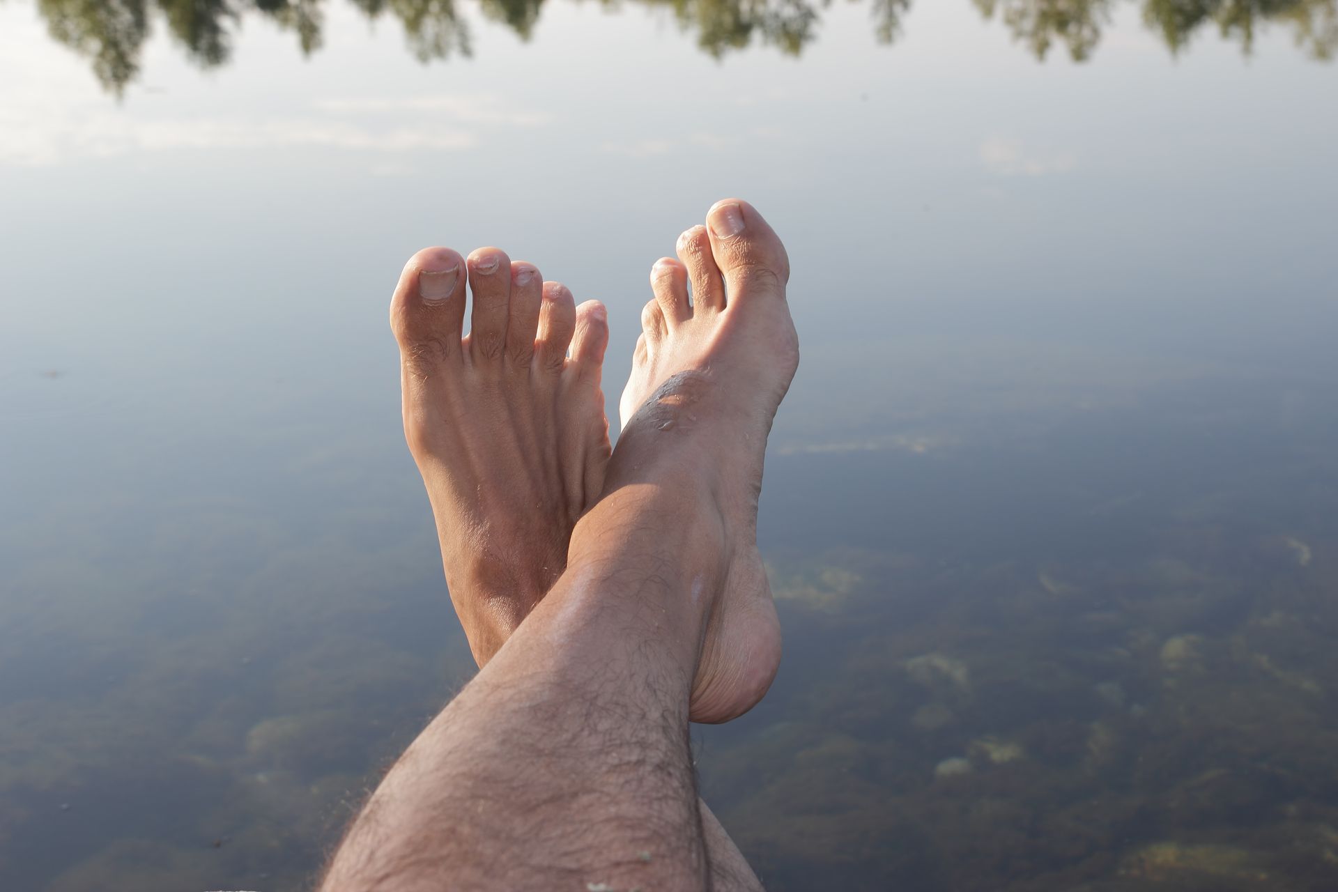 Bare feet crossed, resting by a calm lake.