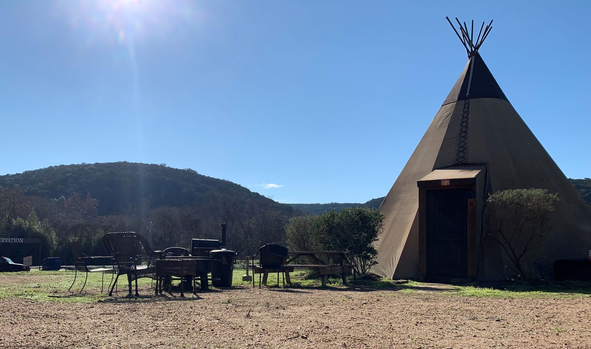 Tipi in sunny field with a mountain backdrop and outdoor seating.