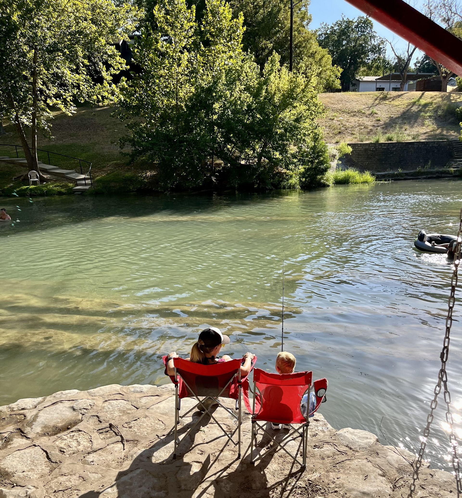 Two people in red chairs by a clear river, enjoying a sunny day outdoors.