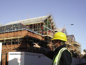 A man in a hard hat and high vis jacket pointing at a property with scaffolding around it 