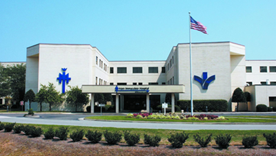St. Joseph's Hospital, a two-story building with a blue cross and logo on a sunny day with an American flag.