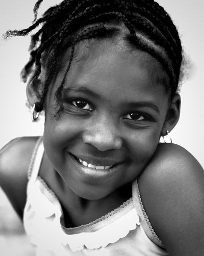 Girl with braided hair smiles, wearing a tank top, looking at the camera.