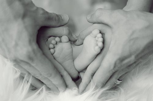 Hands forming a heart around a baby's tiny feet on a fluffy surface.