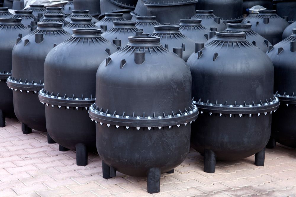 A bunch of black containers are stacked on top of each other on a brick floor.