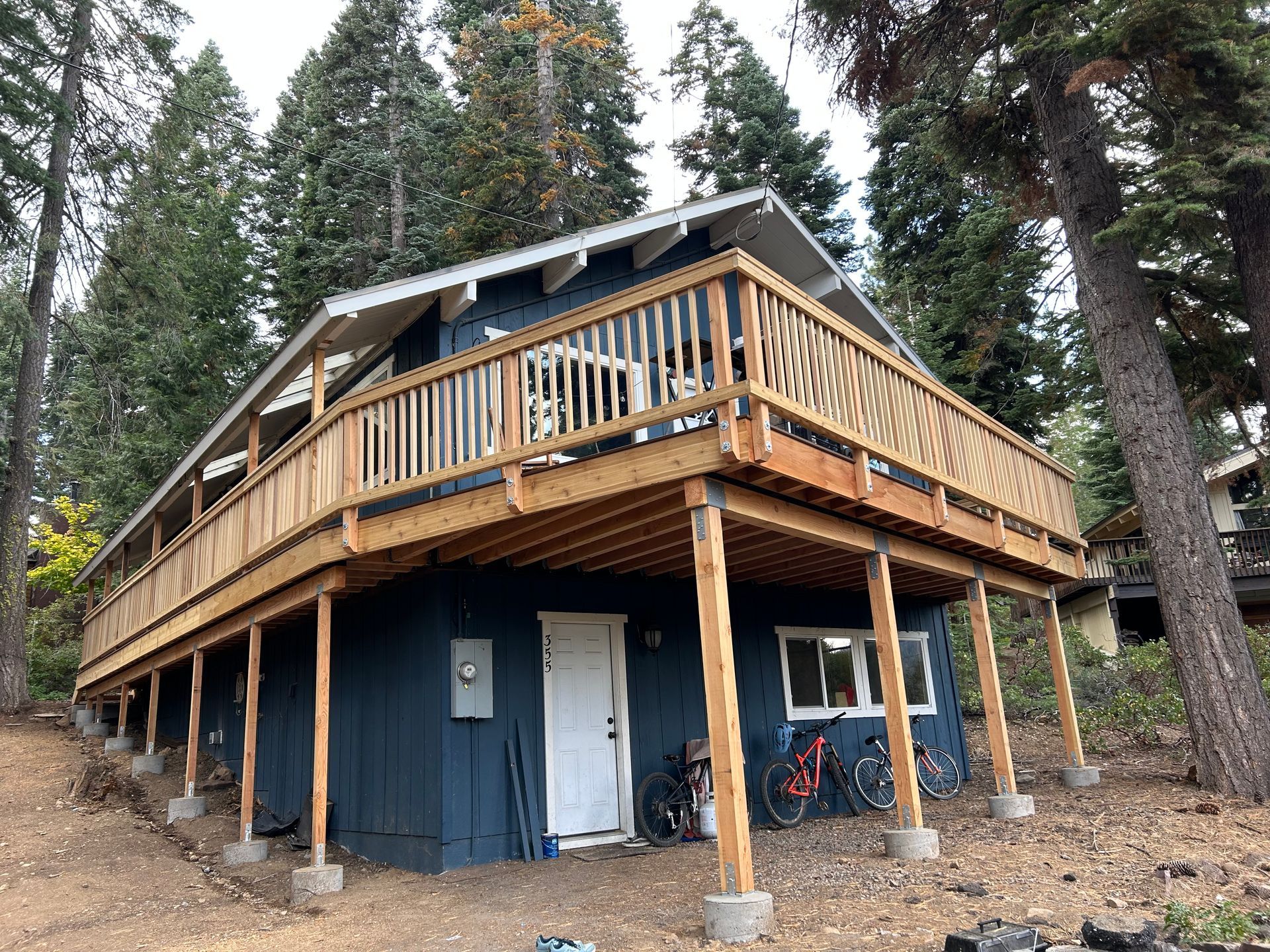 A blue house with a large wooden deck is surrounded by trees.
