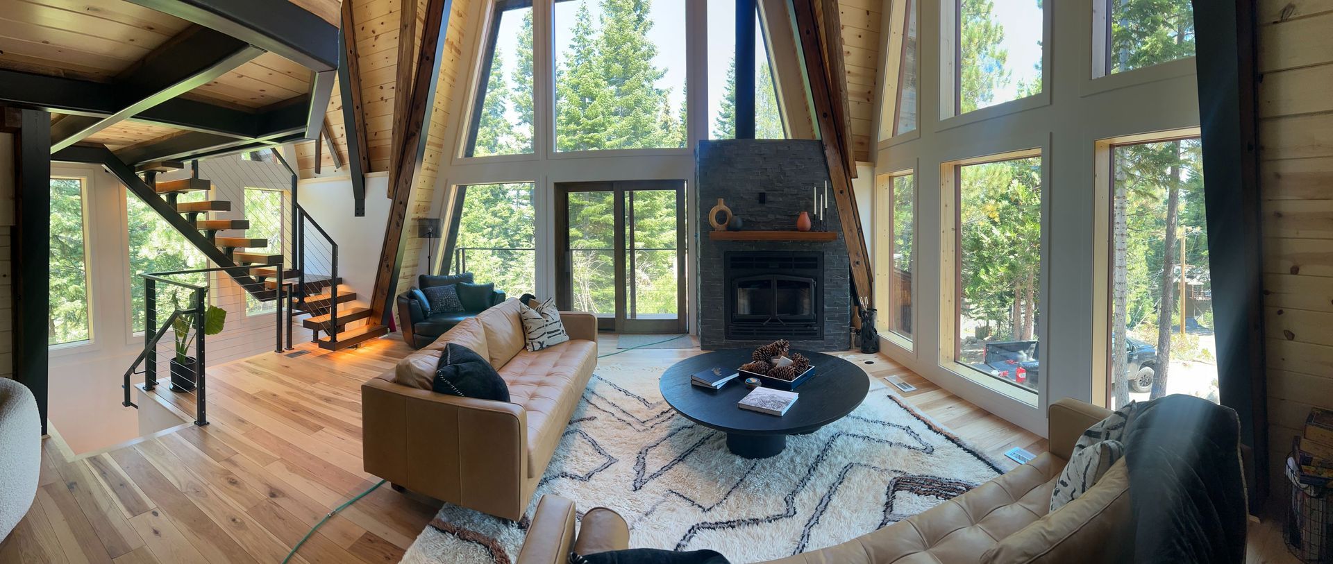 Interior of a modern A-frame cabin with large windows, fireplace, and spiral staircase.