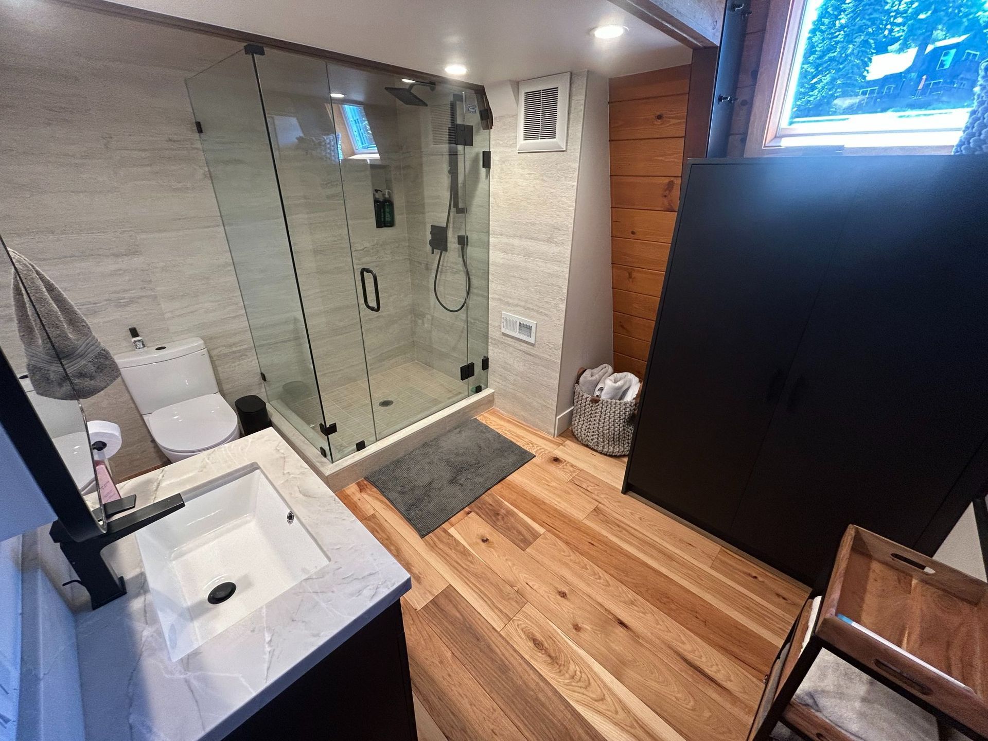 Bathroom with shower, toilet, sink, hardwood floor, and a black cabinet.