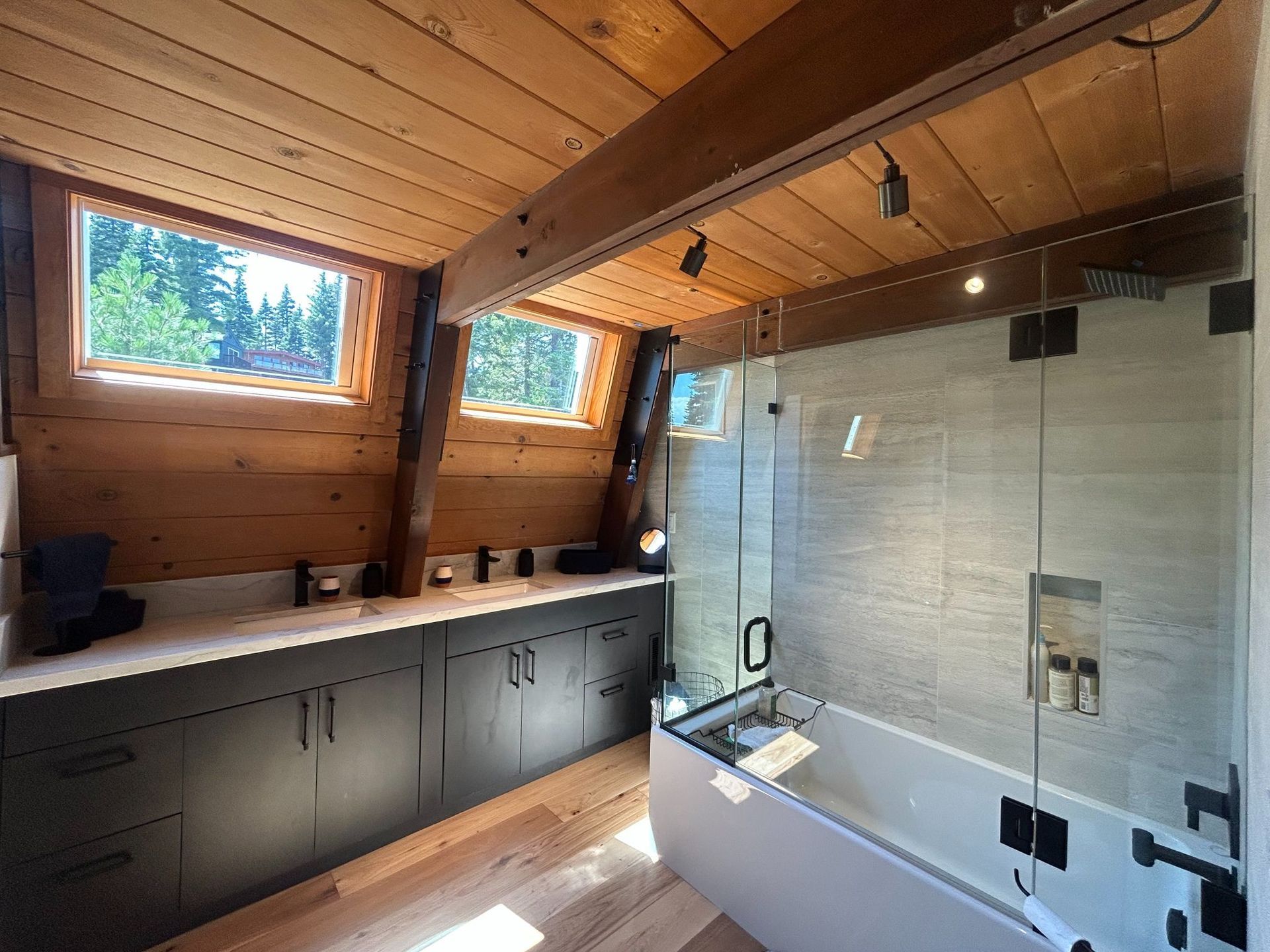 Bathroom with wood paneled walls and ceiling, dark cabinets, a shower with glass doors, and a window.