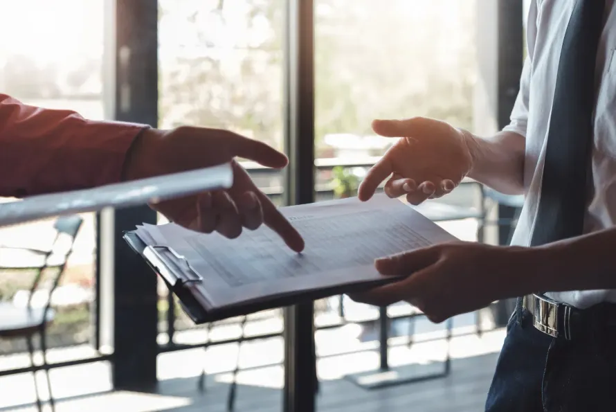 A man is pointing at a piece of paper while another man holds a clipboard.