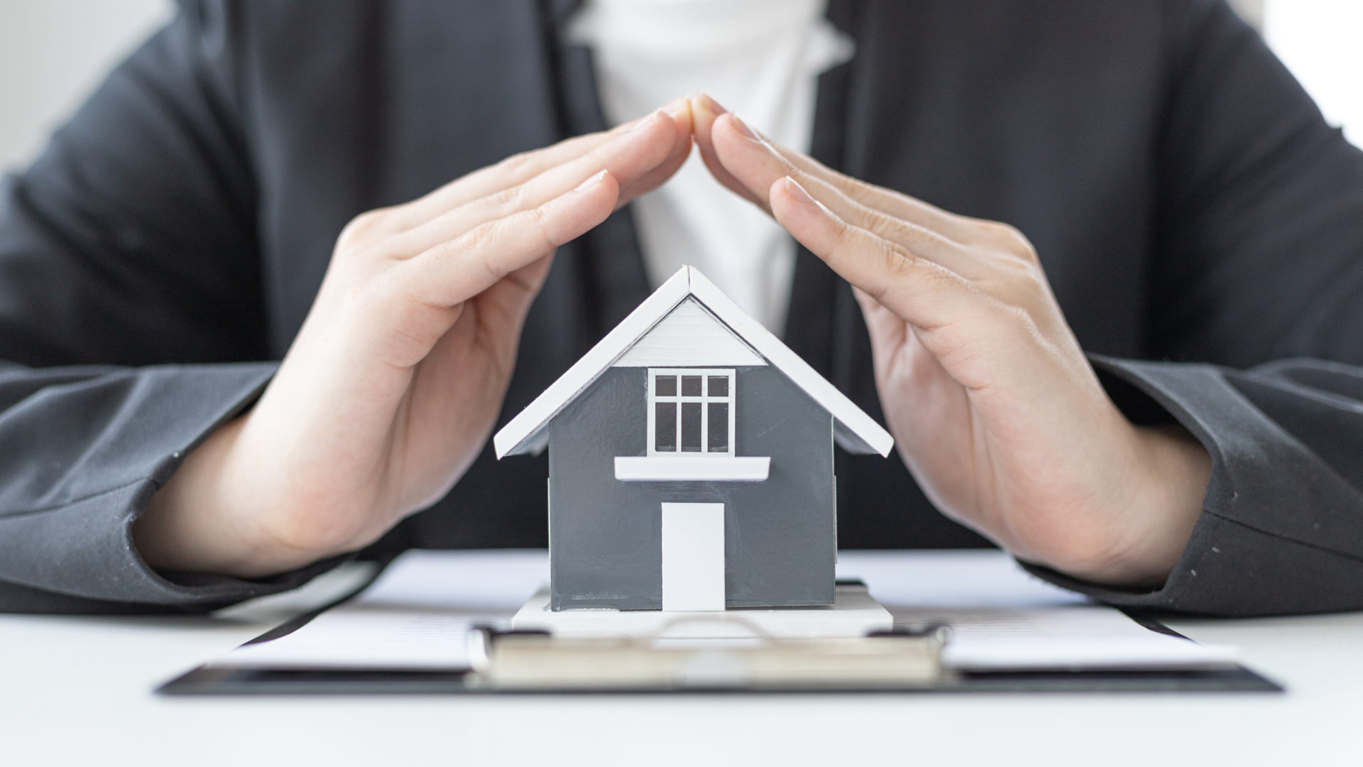 A woman is covering a model house with her hands.