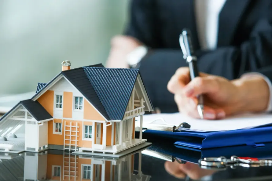 A person is writing on a clipboard next to a model house.