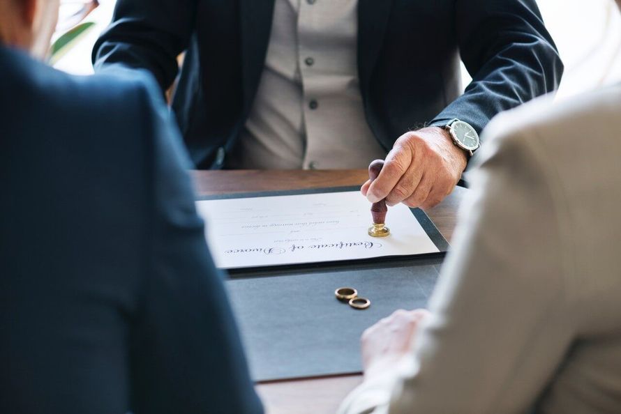 A man is stamping a document with a wax seal while sitting at a table with two people.