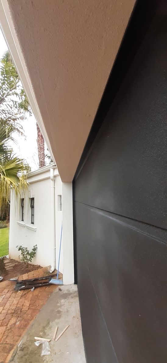 A dark garage door next to a white building with beige trim.