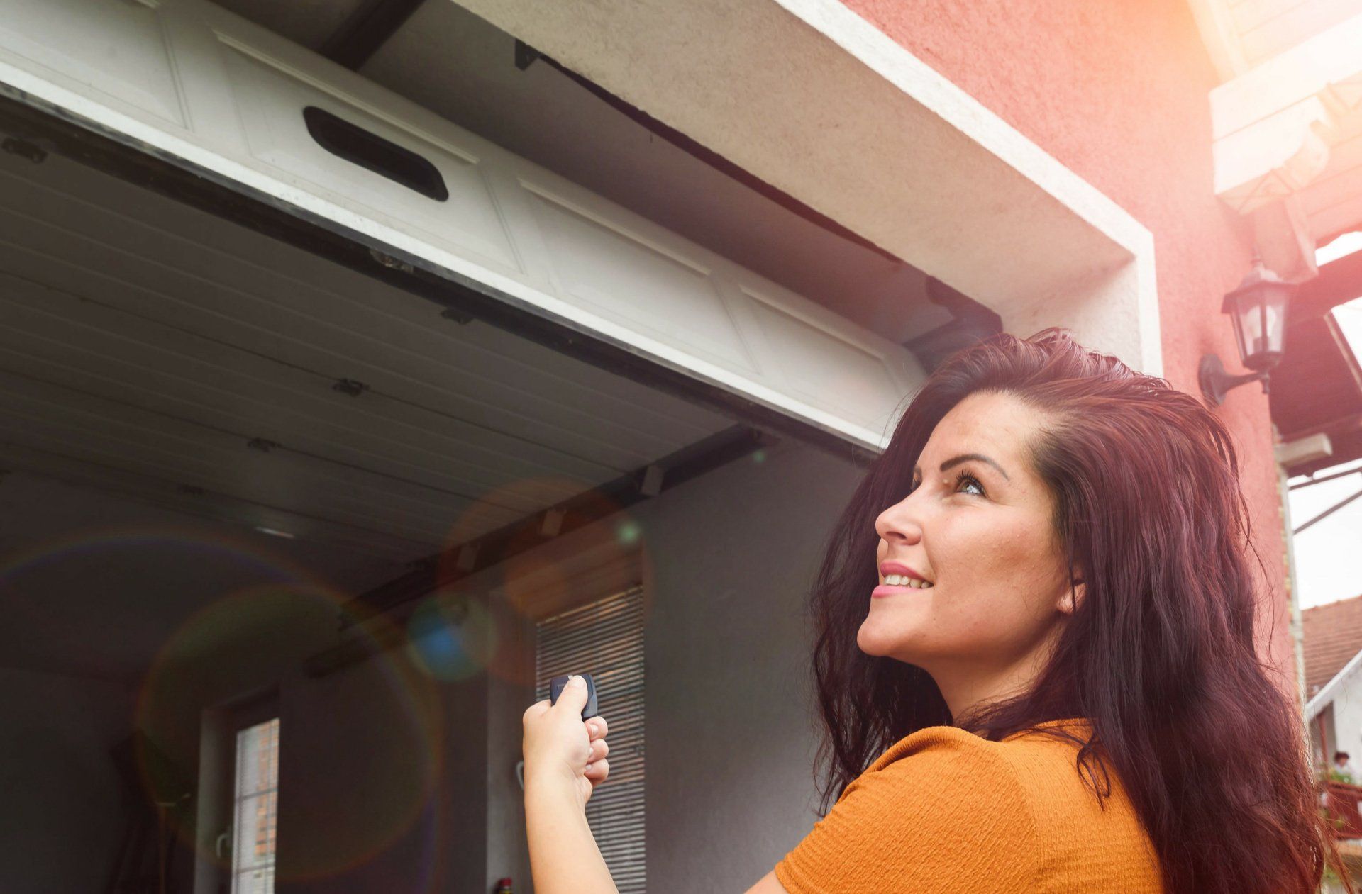 woman standing in front of a sectional garage door with a garage door remote in her hand