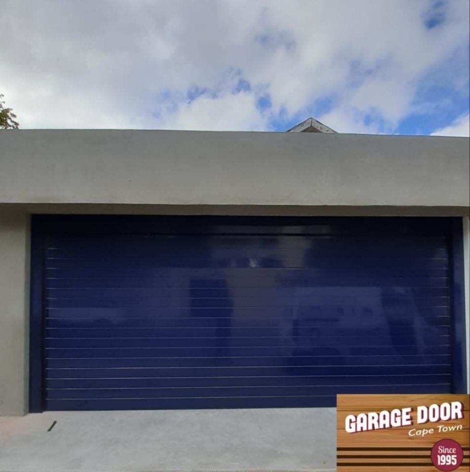 Blue garage door on a gray building against a partly cloudy sky.