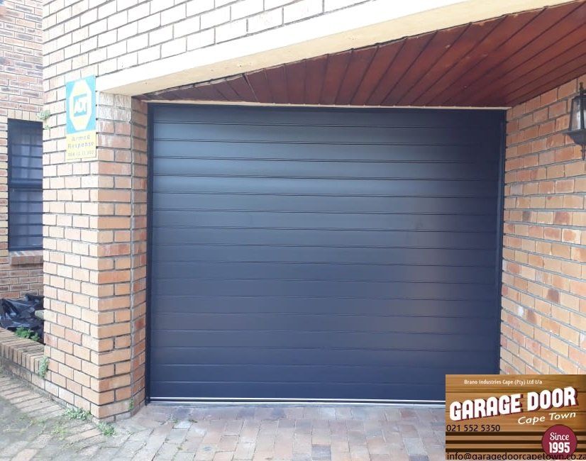 Dark gray horizontal-slat garage door in brick building. Sign above, text: Garage Door.
