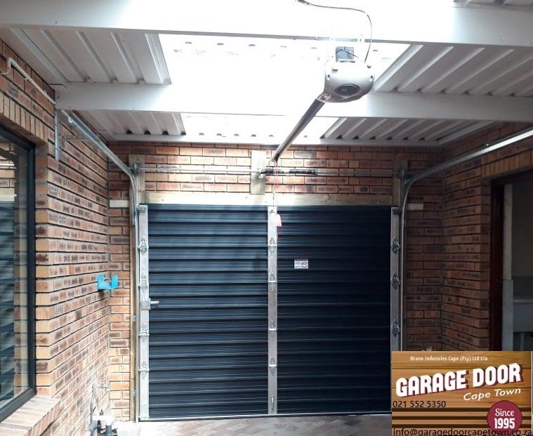 Brick garage with a closed black door, automated opener, and the Garage Door Cape Town logo.