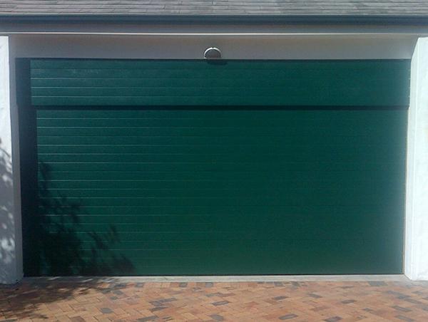 Green garage door with white trim, mounted on a brick driveway.