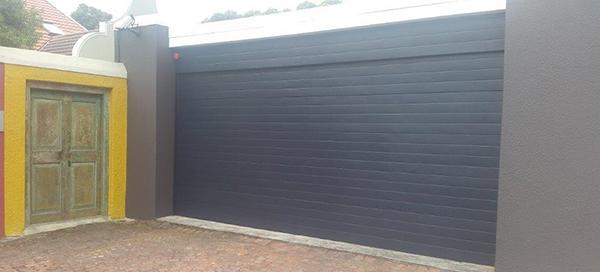 A gray gate next to a yellow and brown building with an aged green door.
