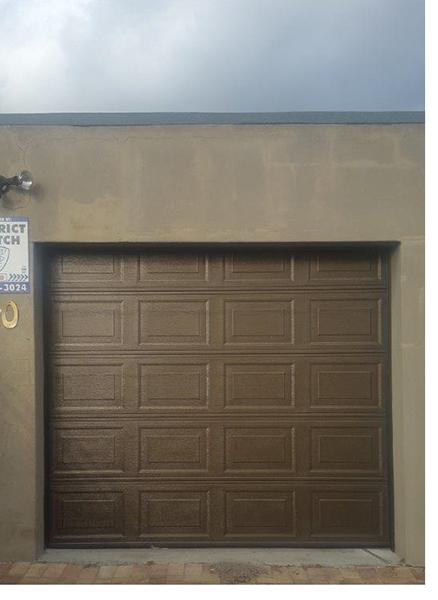 Brown garage door on a tan building under a cloudy sky.
