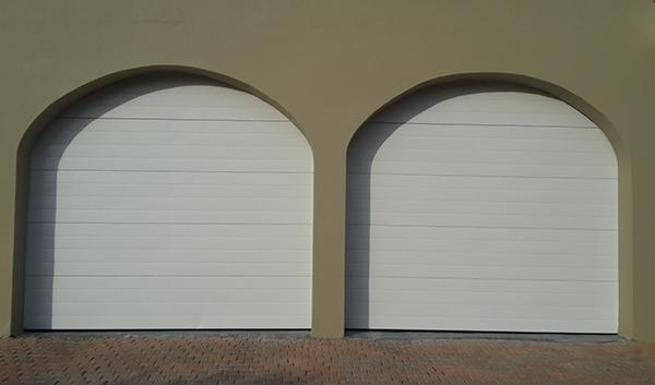 Two arched, white garage doors set in a tan wall.