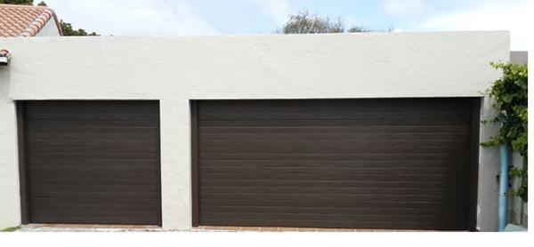 Two dark brown garage doors in a white building.