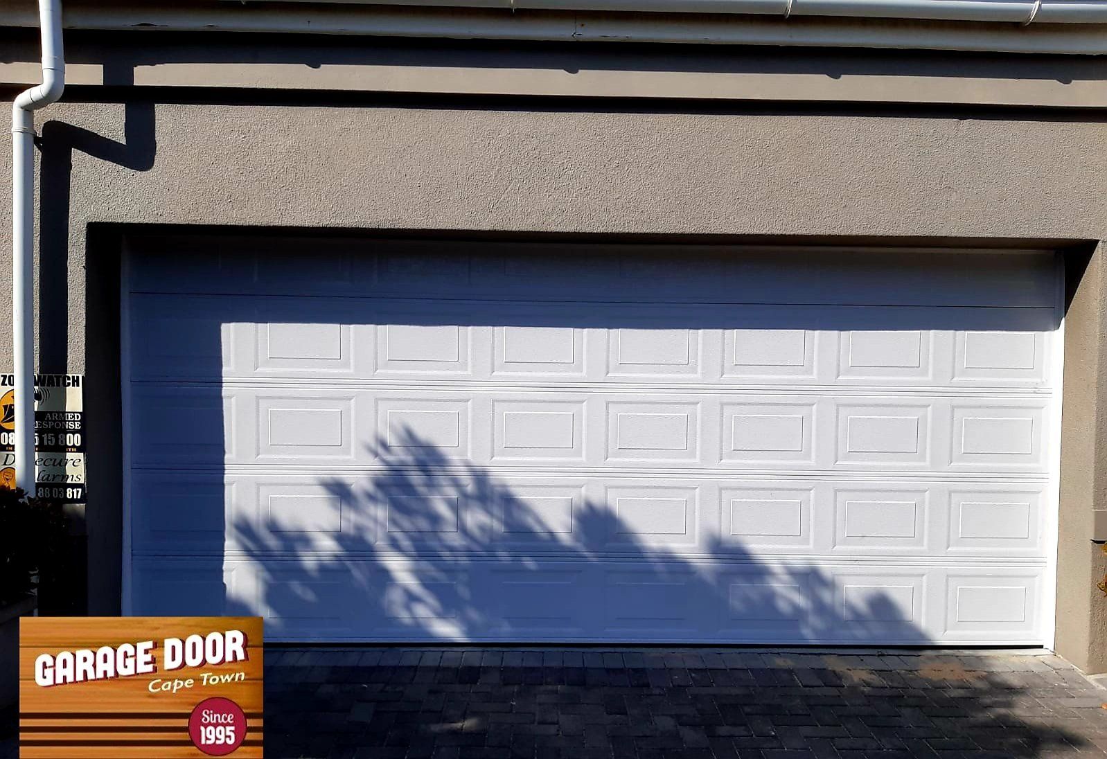 White garage door with square panels, casting shadows, in a building's exterior.