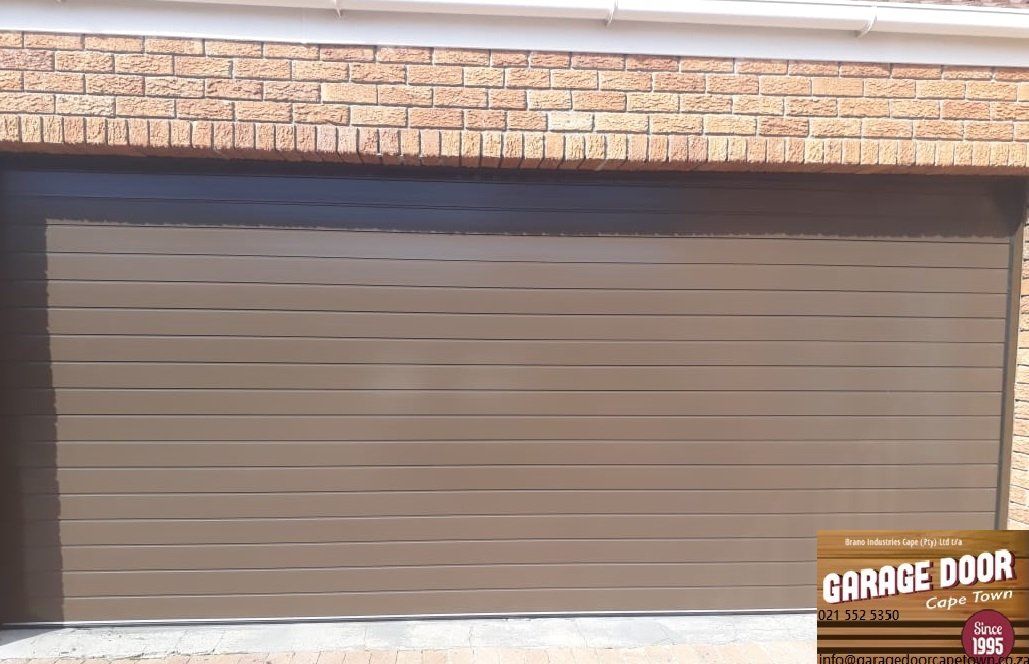 Brown garage door with horizontal lines, set in a brick wall with a white trim.