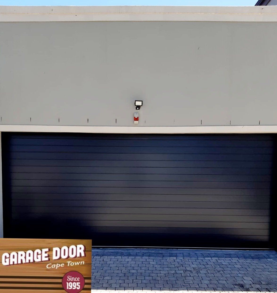 Black garage door on a grey building with paving.