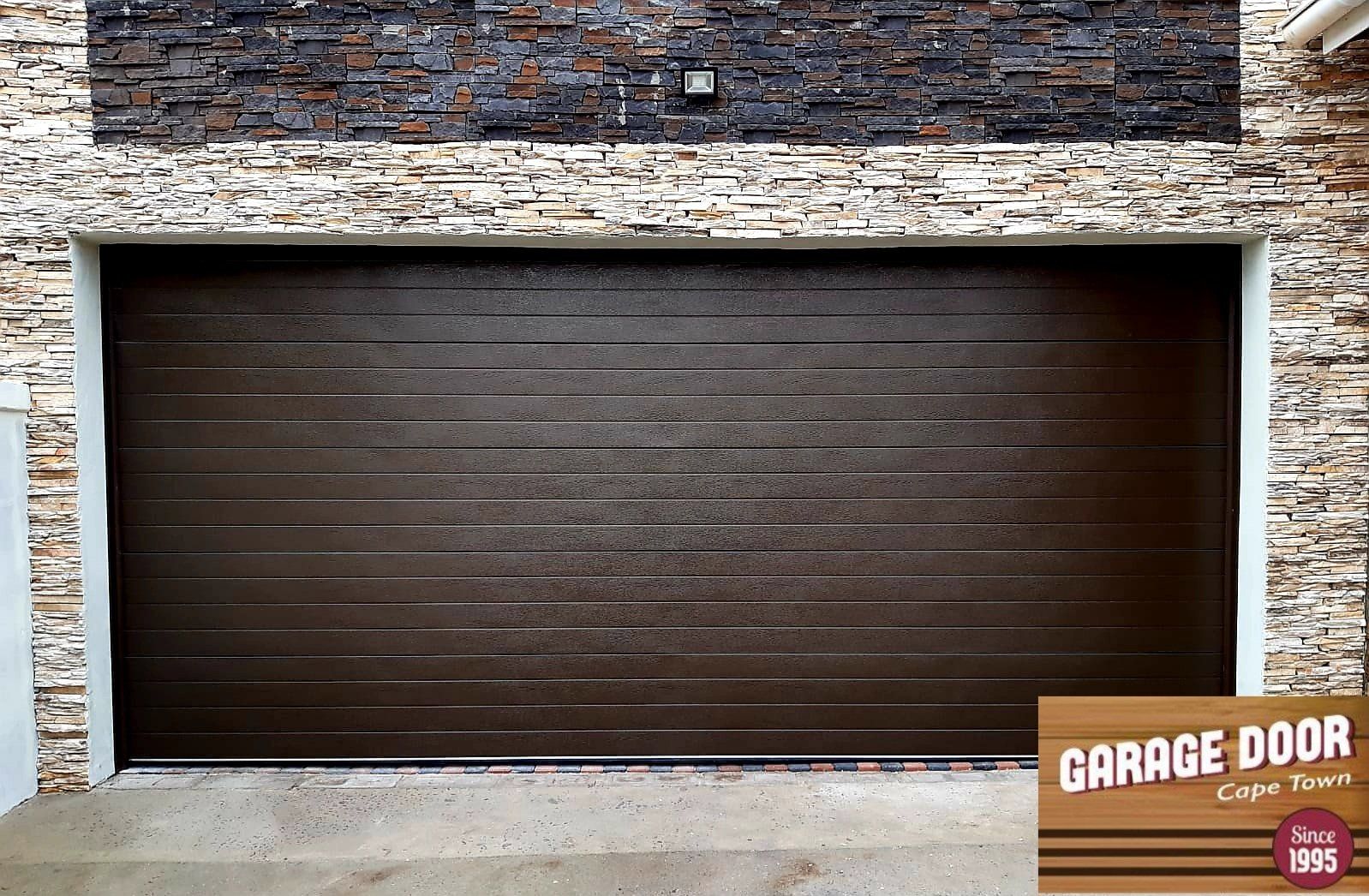 Brown garage door with horizontal lines set in a stone exterior;