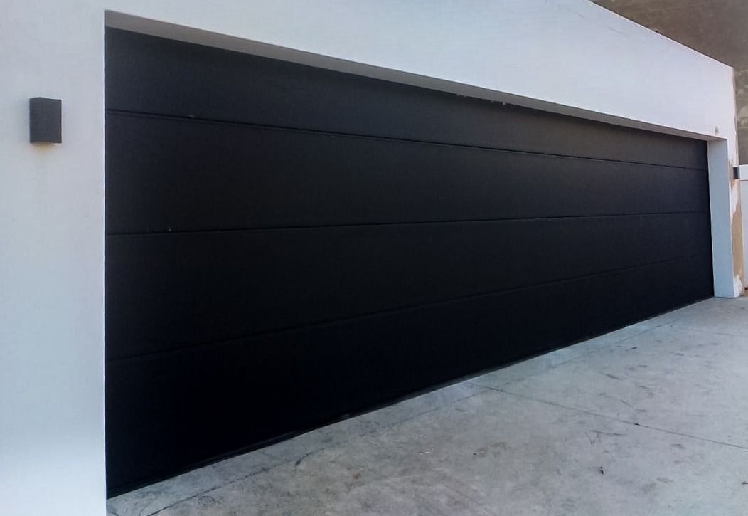 Black garage door on a white building, set against a concrete driveway.