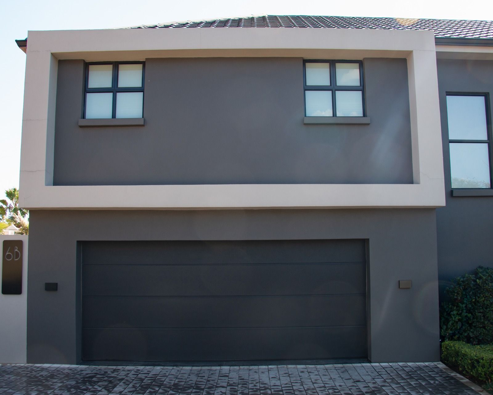 Gray house facade with two windows inside a cream-colored rectangle, above a closed garage door.
