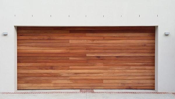 Wooden garage door set in a white wall, with two lights and brickwork at the bottom.